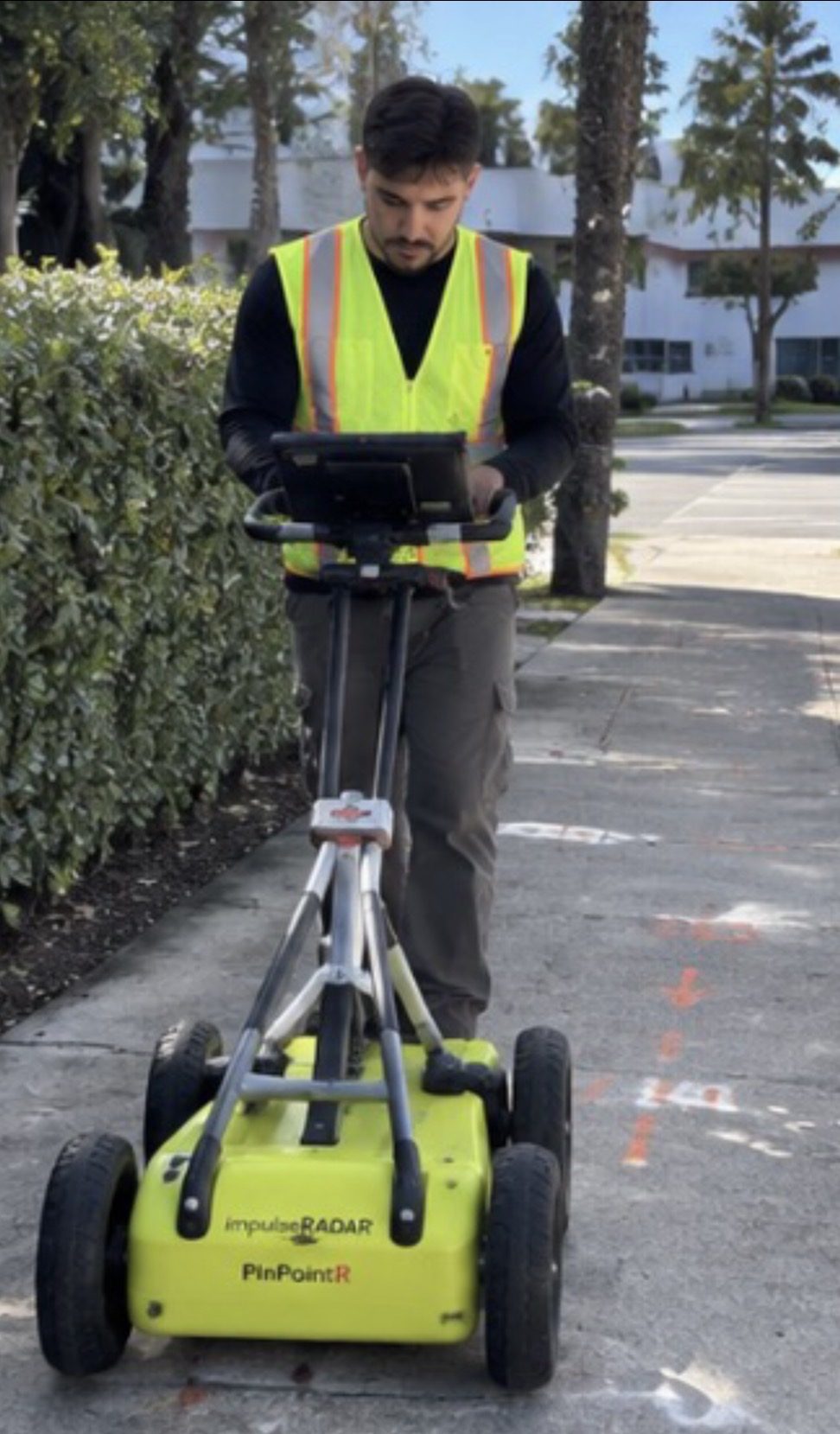 US Utility Potholing technician running a GPR cart along a sidewalk in South Florida