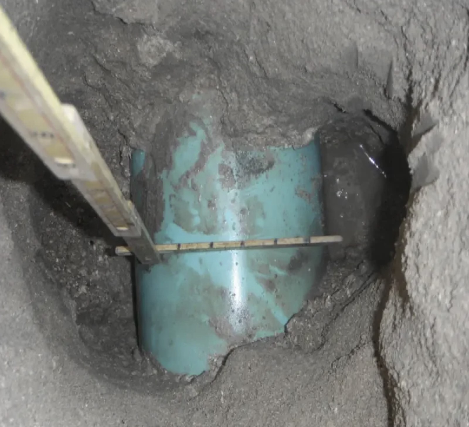 Exposed pipe in an open test hole with depth to top of pipe being measured