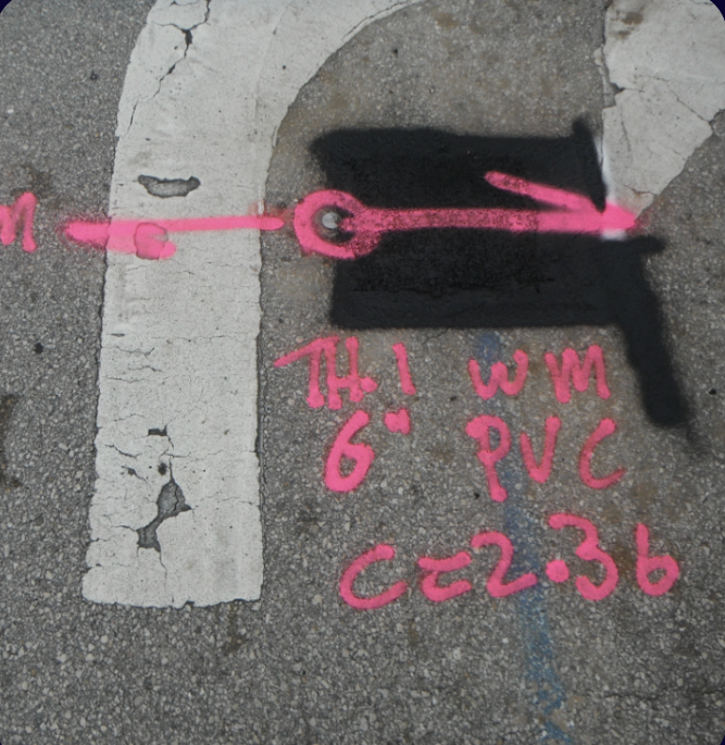 Pink spray paint marks on concrete showing pothole test data — Th1 Wm 6-inch PVC — construction potholing documentation South Florida